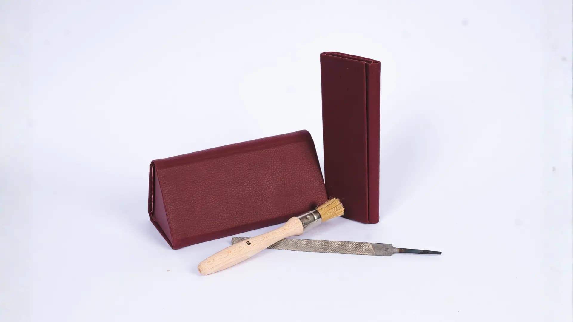 Luxury leather eyewear cases displayed with traditional leather crafting tools on clean white background