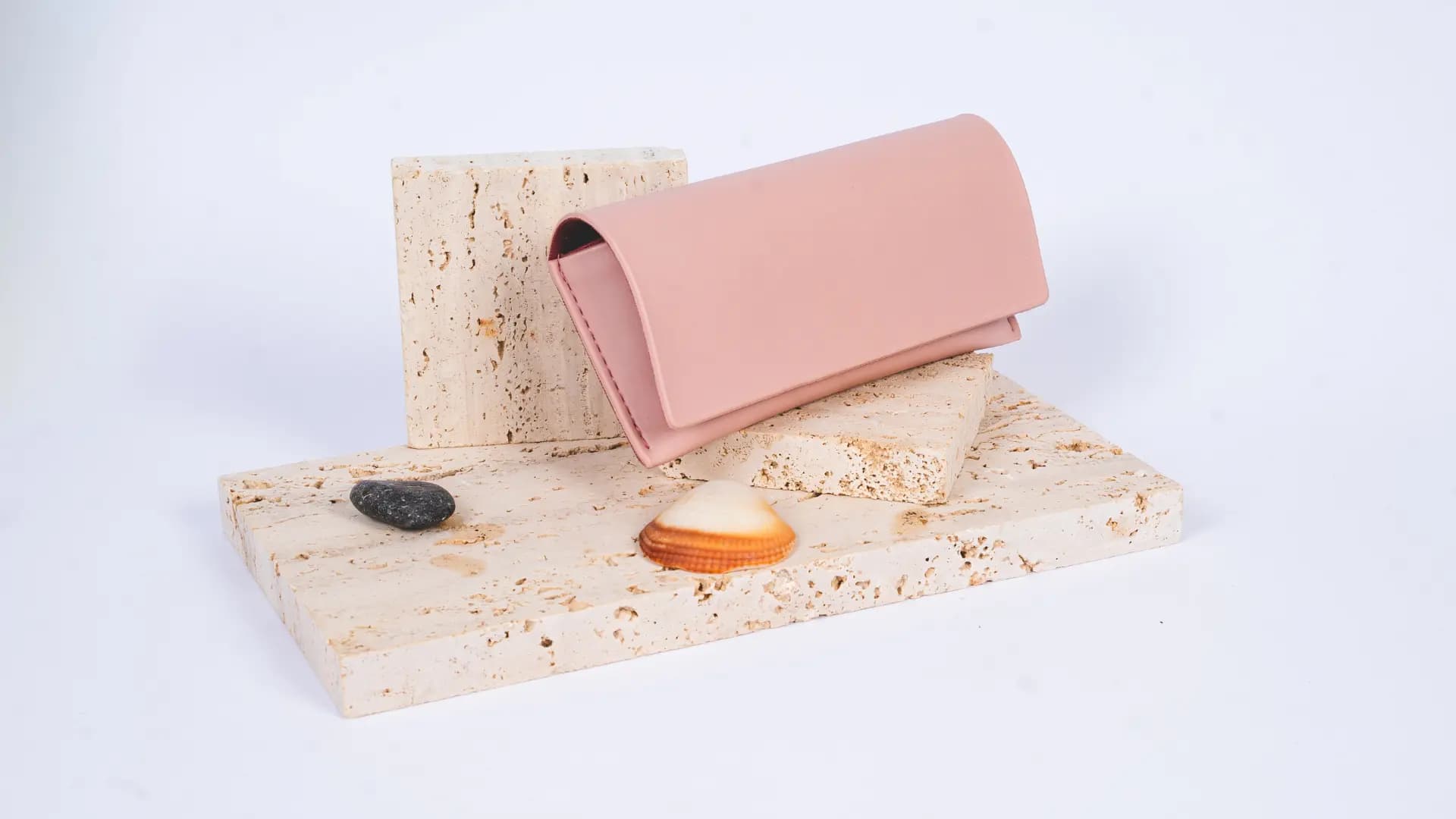 Luxury eyewear case resting on natural seashells and travertine stone, highlighting organic textures and premium finish